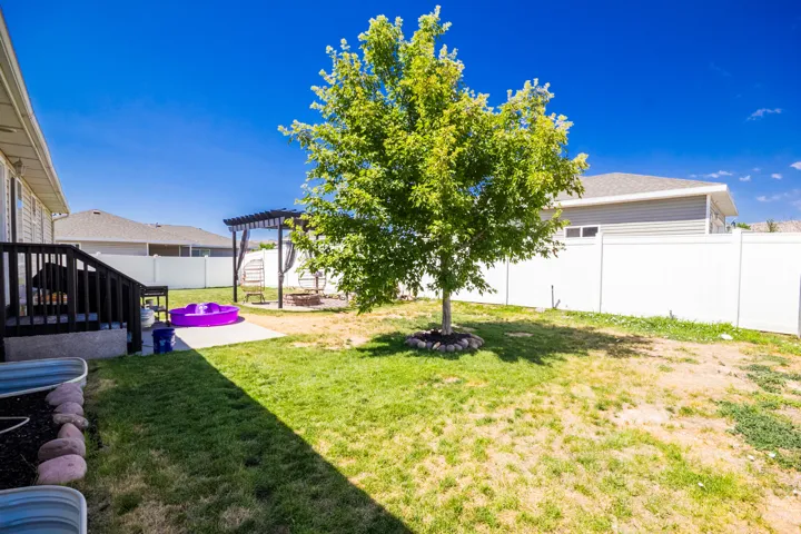 Expansive backyard featuring a mature tree, a privacy fence, and a concrete patio with a dark wood pergola