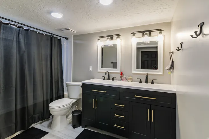 Dual vanity with black cabinetry, brass hardware, and white countertops