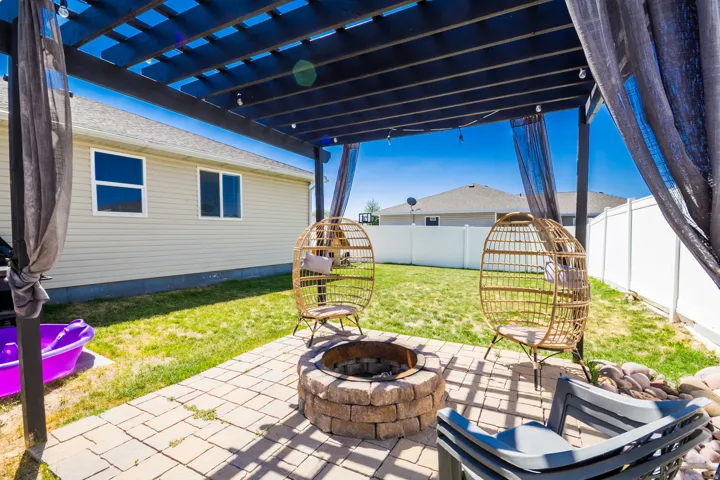 Outdoor patio featuring a stone-look fire pit, paver flooring, and a dark-stained wood pergola with string lights