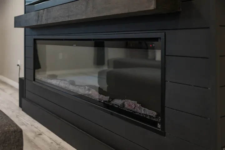 Built-in linear electric fireplace with a black shiplap surround and a wood-finish mantel