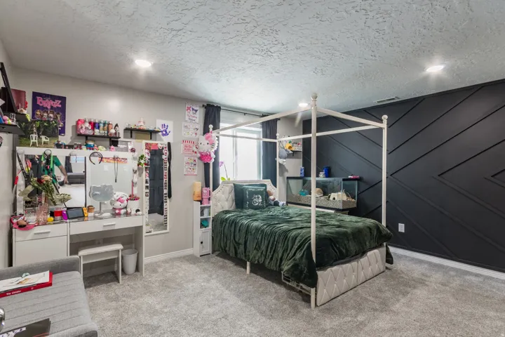 Bedroom featuring textured gray carpeting, a dark accent wall with geometric paneling, and recessed ceiling lighting