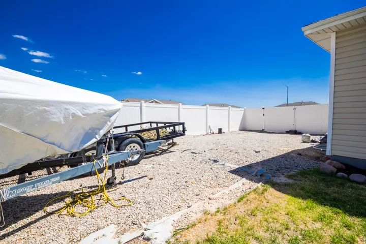 Spacious gravel yard area with full white privacy fencing, featuring a side access gate and a partial view of the property's exterior siding