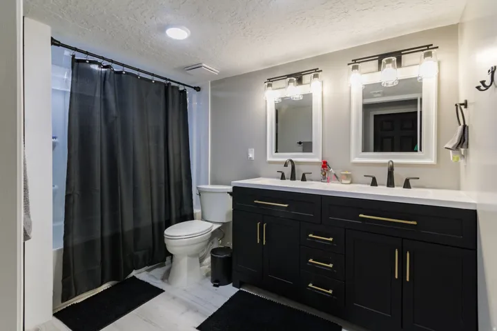 Double vanity featuring black cabinetry with gold-finish hardware, individual framed mirrors, and wall-mounted light fixtures