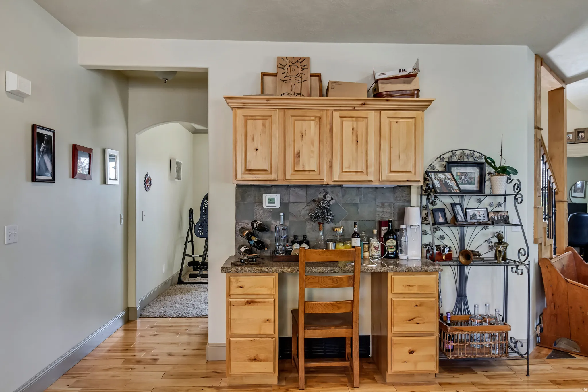 Built-in cabinetry with a stone-look backsplash, light wood-finish flooring, a built-in desk area with a granite-look countertop, and an arched hallway entry