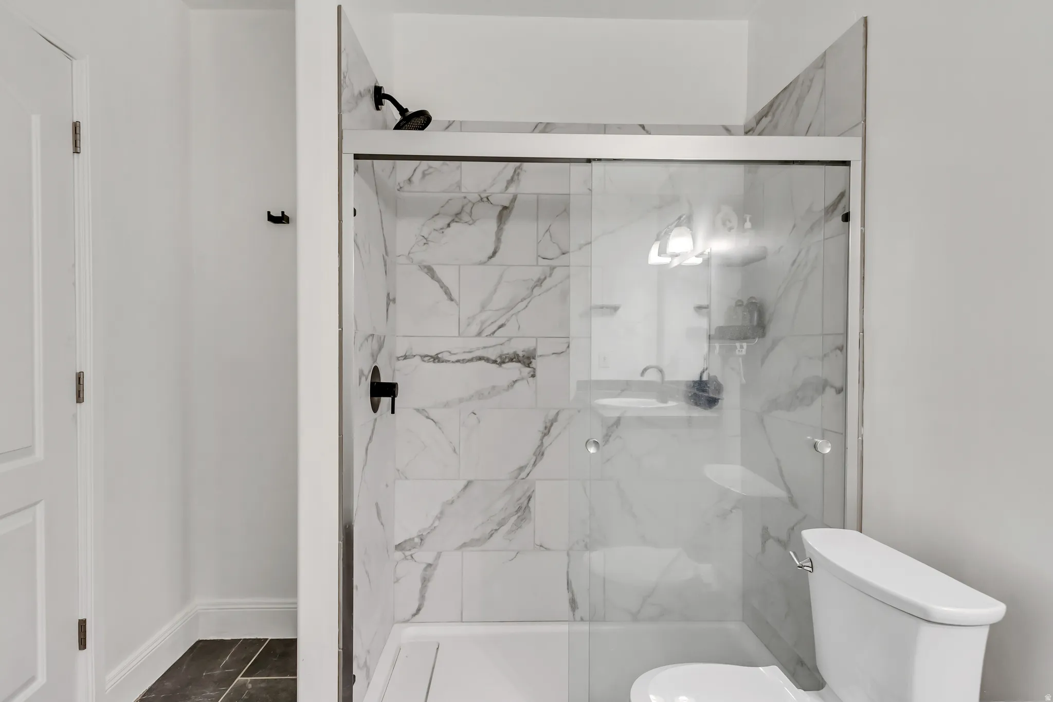 Shower with sliding glass doors, white subway tile surround with gray veining, matte black shower fixtures, and integrated shelving