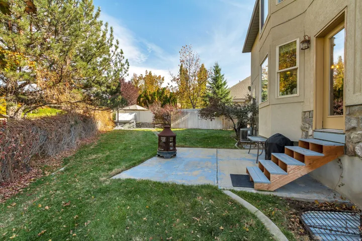 Spacious backyard featuring a concrete patio, exterior access stairs with wood treads, and a stucco and stone exterior