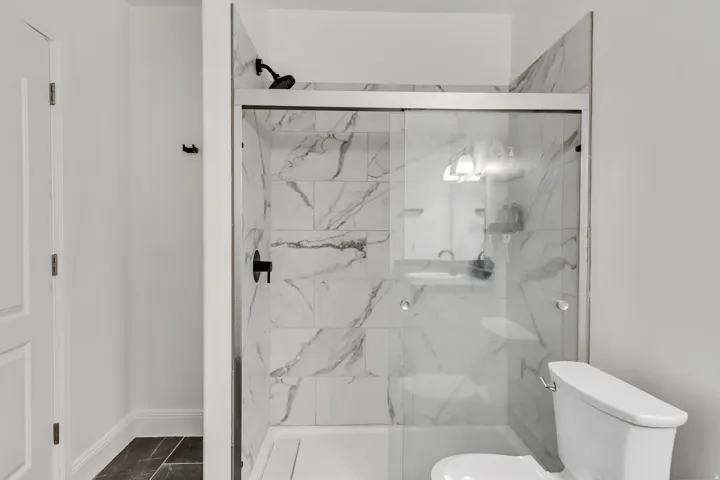 Shower with sliding glass doors, white subway tile surround with gray veining, matte black shower fixtures, and integrated shelving