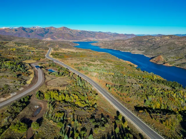 Expansive mountain and water scenery featuring a paved road, a serene body of water, and distant snow-capped peaks