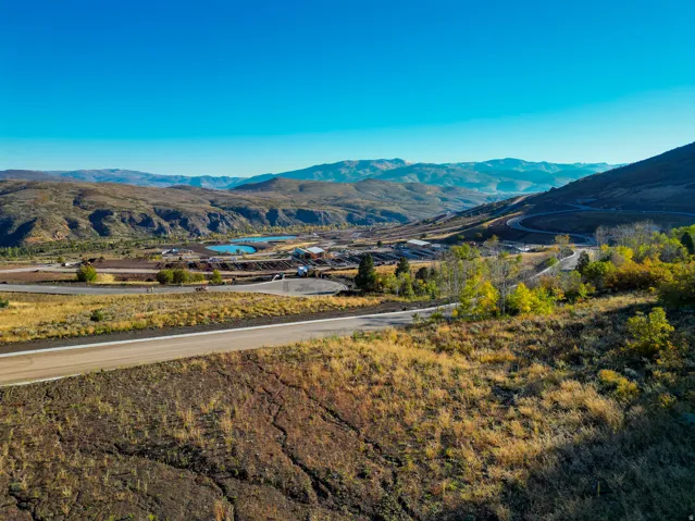 Expansive mountain landscape featuring a winding road, natural bodies of water, and distant structures