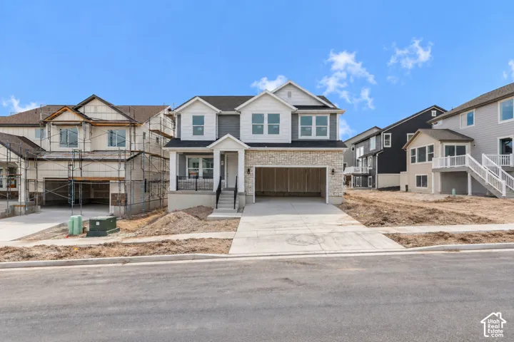 Two-story residence featuring a covered front porch, stone and siding exterior, attached garage, and concrete driveway