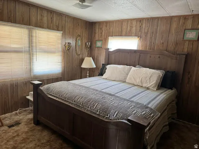 Wood-paneled room featuring two windows with horizontal blinds, textured ceiling, and plush carpeting