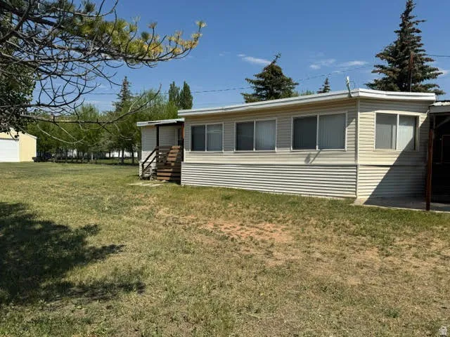 Spacious property featuring a light-colored mobile home with horizontal siding, multiple windows, and a raised wooden entry deck with stairs