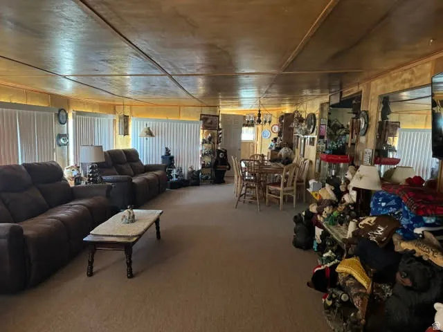 Open concept living and dining area featuring carpet flooring, panel walls, and a panel ceiling with exposed beams