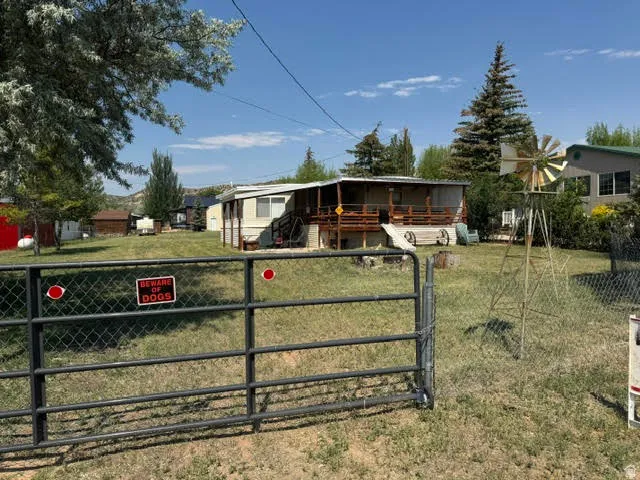 Expansive property featuring a chain-link fence and metal gate, a large yard with mature trees, and a visible windmill structure