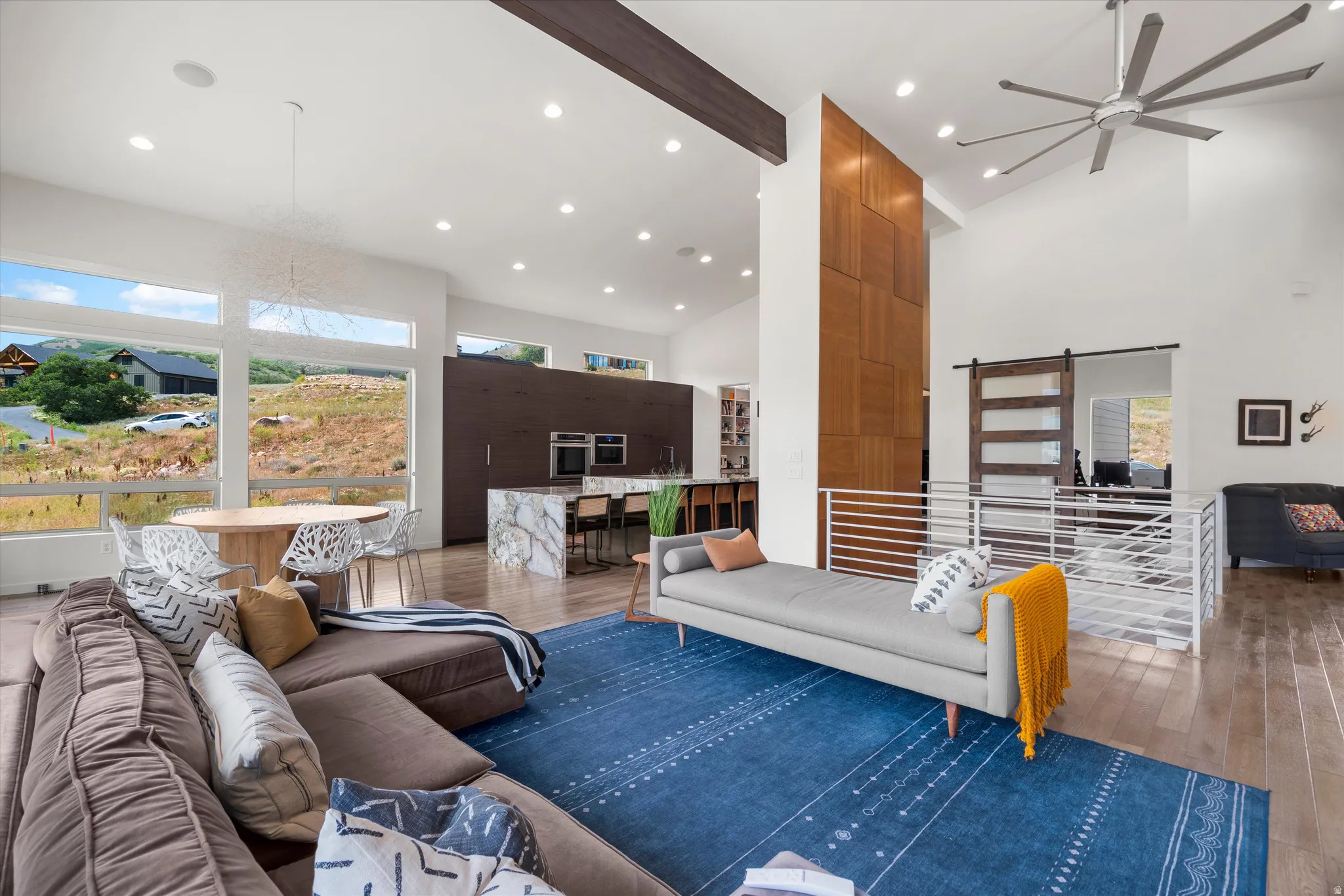 Great room featuring vaulted ceilings, wood-finish flooring, a contemporary ceiling fan, and large picture windows