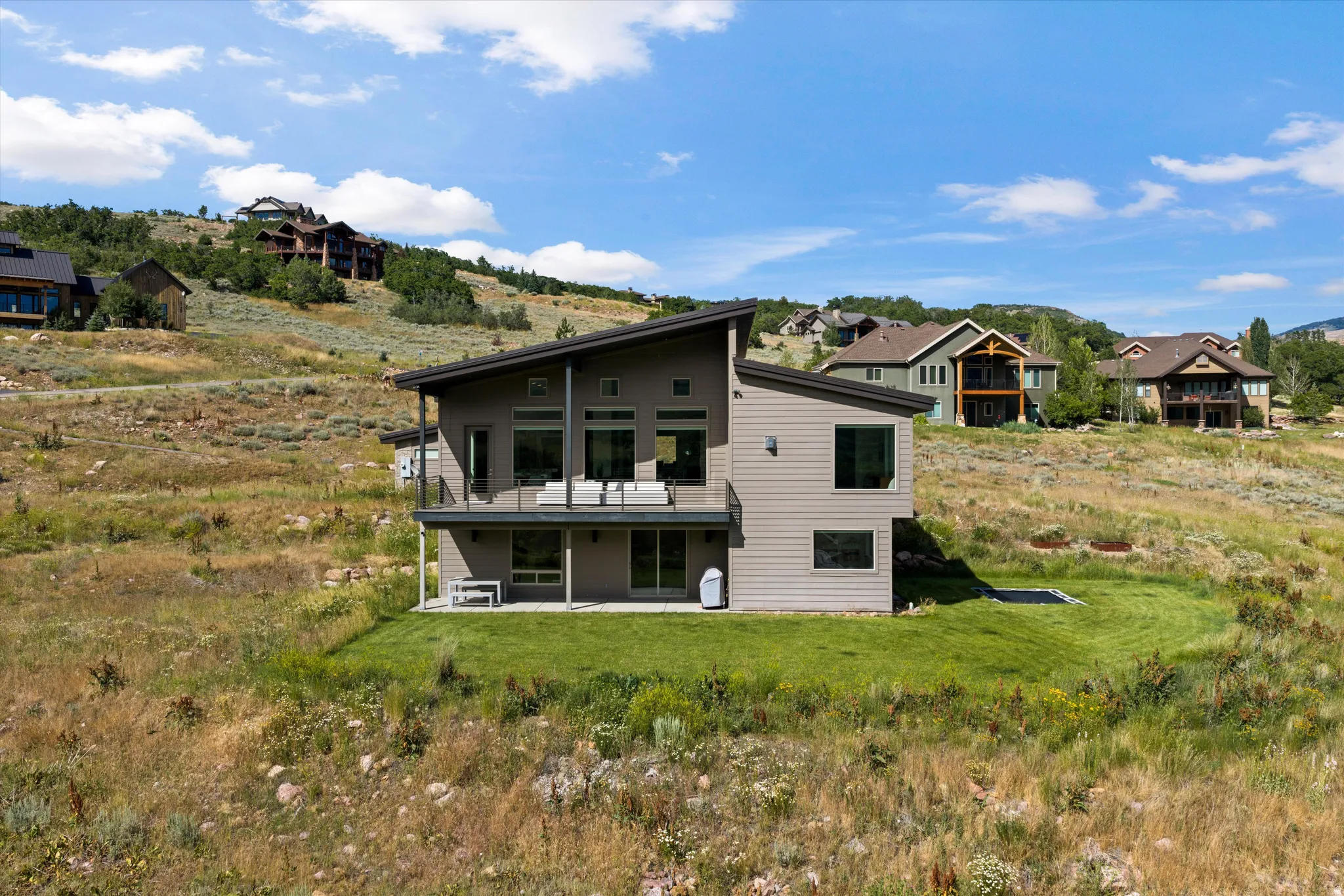 Contemporary architecture featuring a multi-level design, a private balcony with glass railing, and a ground-level patio