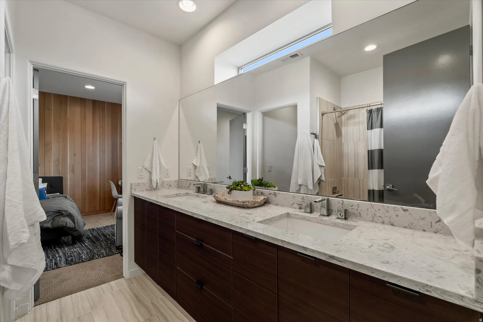 Bathroom featuring a dual-sink vanity with a light-toned countertop, wood-finish cabinetry, and a large wall-mounted mirror