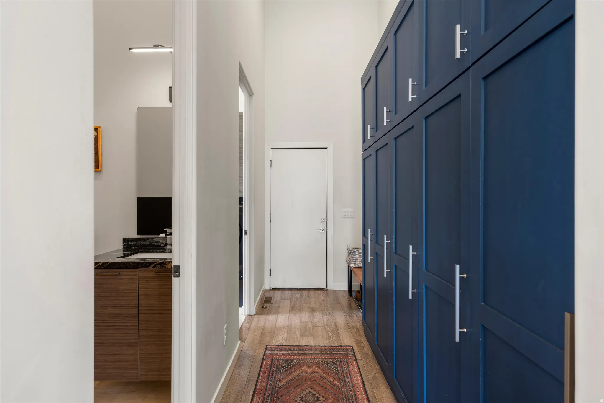 Hallway featuring floor-to-ceiling blue cabinetry with silver hardware, wood-finish flooring, and a high ceiling