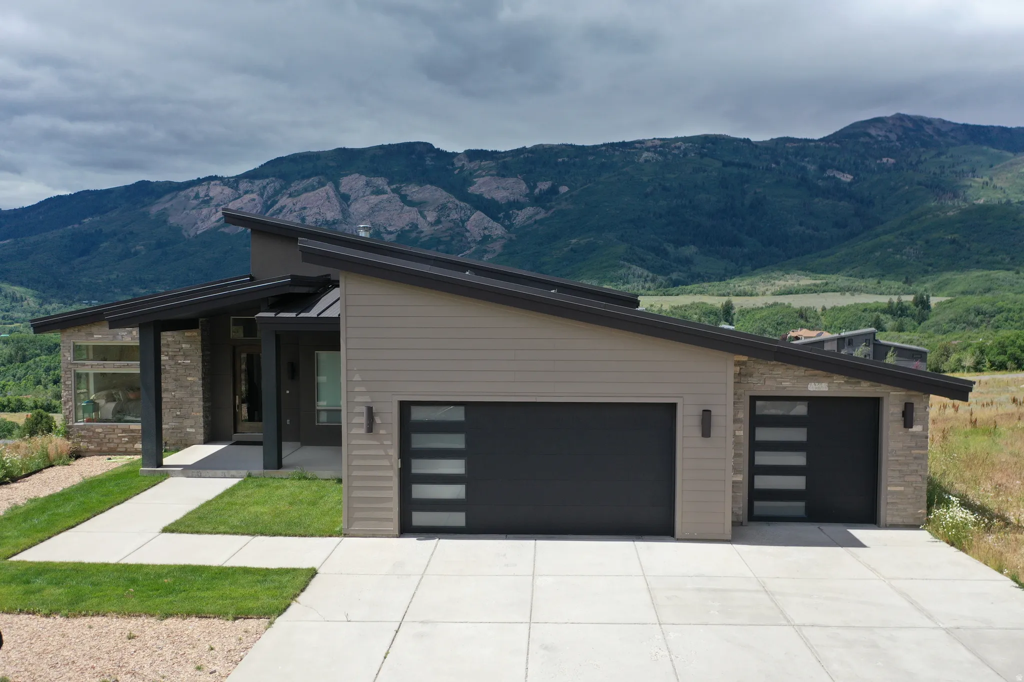 Modern home exterior featuring multiple garage doors with frosted glass panels, an angled roofline, and stone veneer accents