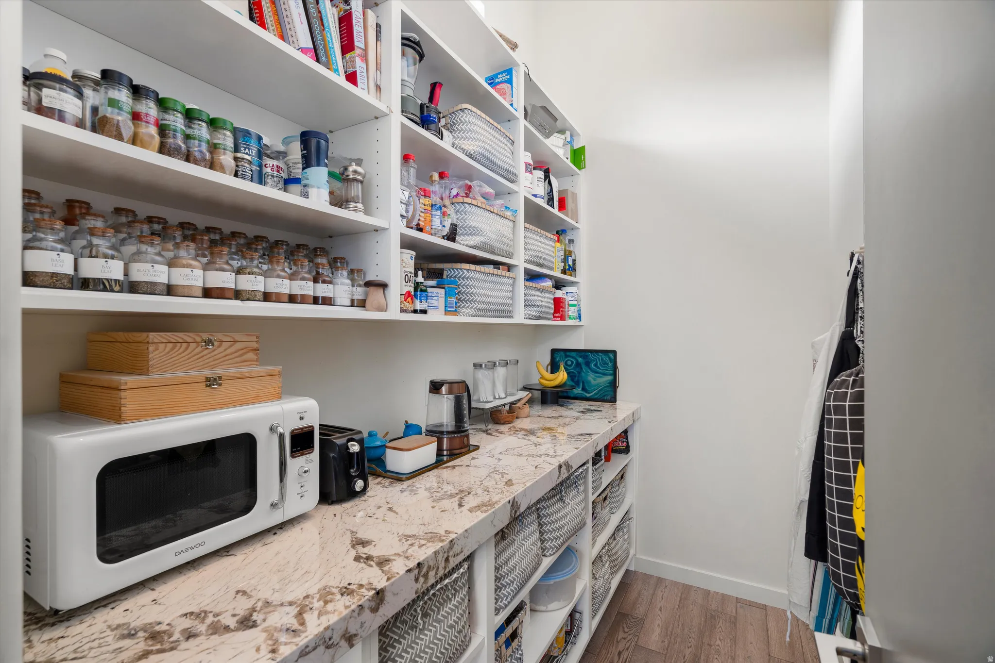 Walk-in pantry featuring extensive built-in shelving, a spacious countertop, wood-finish flooring, and white cabinetry