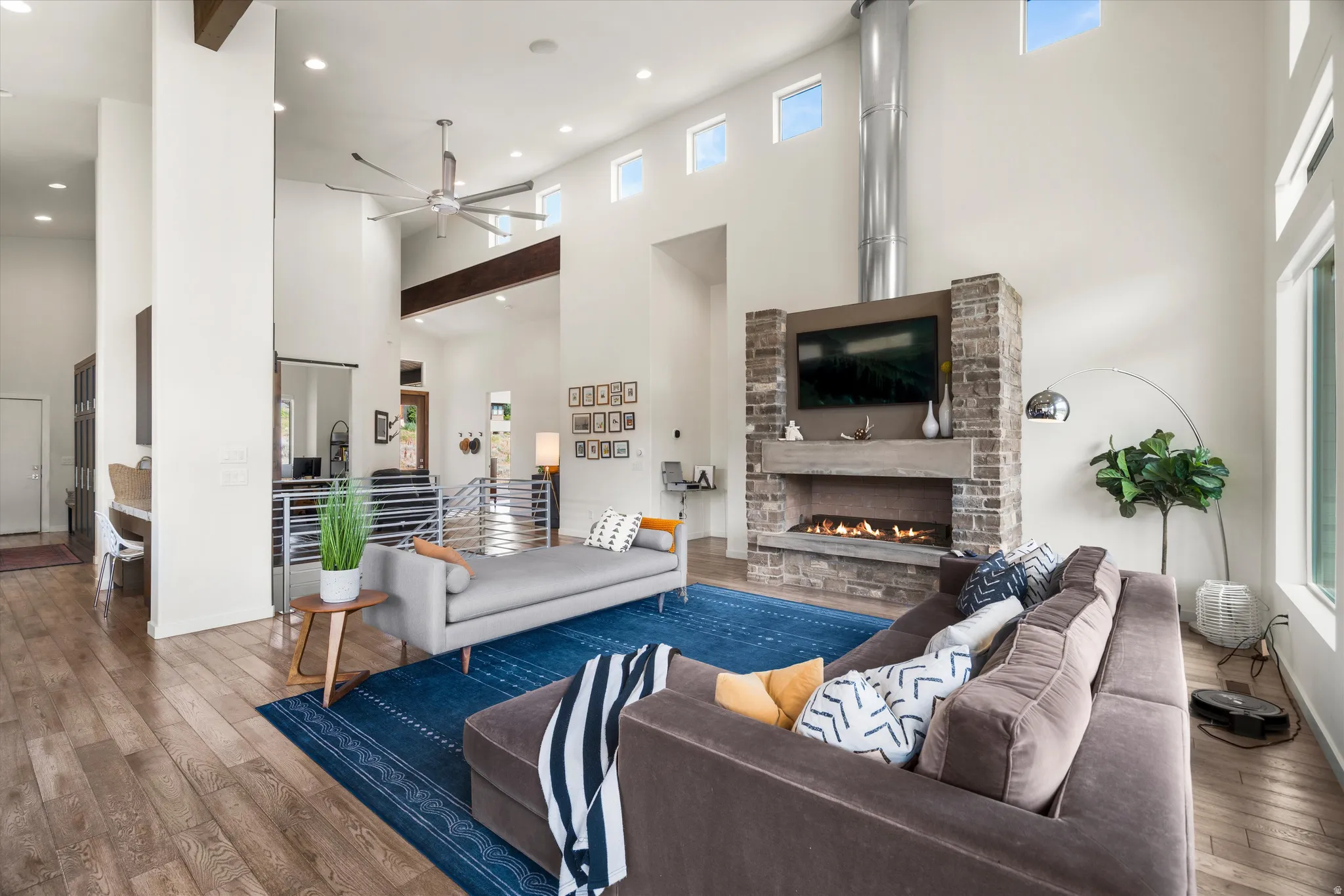 Two-story living area featuring wood-finish flooring, a contemporary stone fireplace with a built-in fire feature, a high ceiling with exposed beams, and multiple clerestory windows