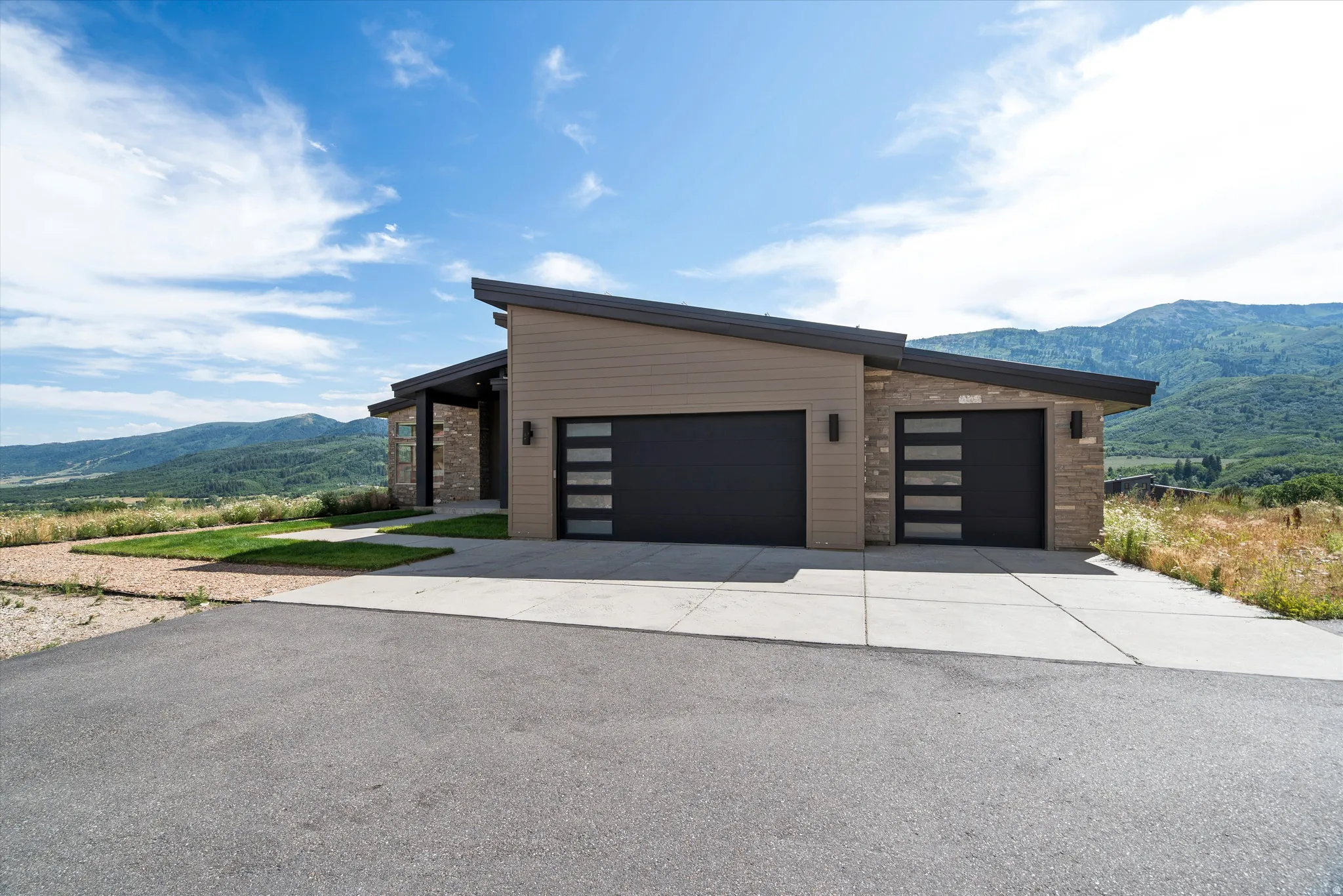 Modern architectural design featuring a sloped roofline, a combination of horizontal siding and stone veneer, and multiple garage doors with frosted glass inserts