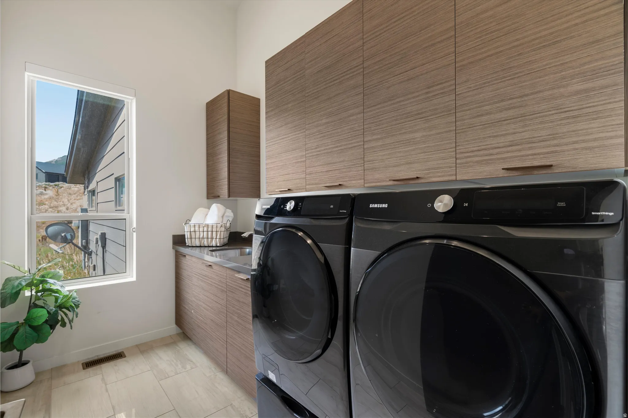 Dedicated laundry area featuring a built-in sink, stone-finish countertop, and ample wood-finish cabinetry