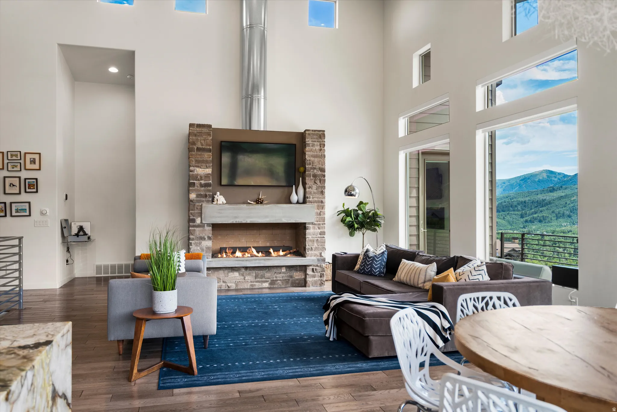 Spacious living area featuring a stone and concrete fireplace with integrated media space, high ceilings, large floor-to-ceiling windows, and wood-finish flooring