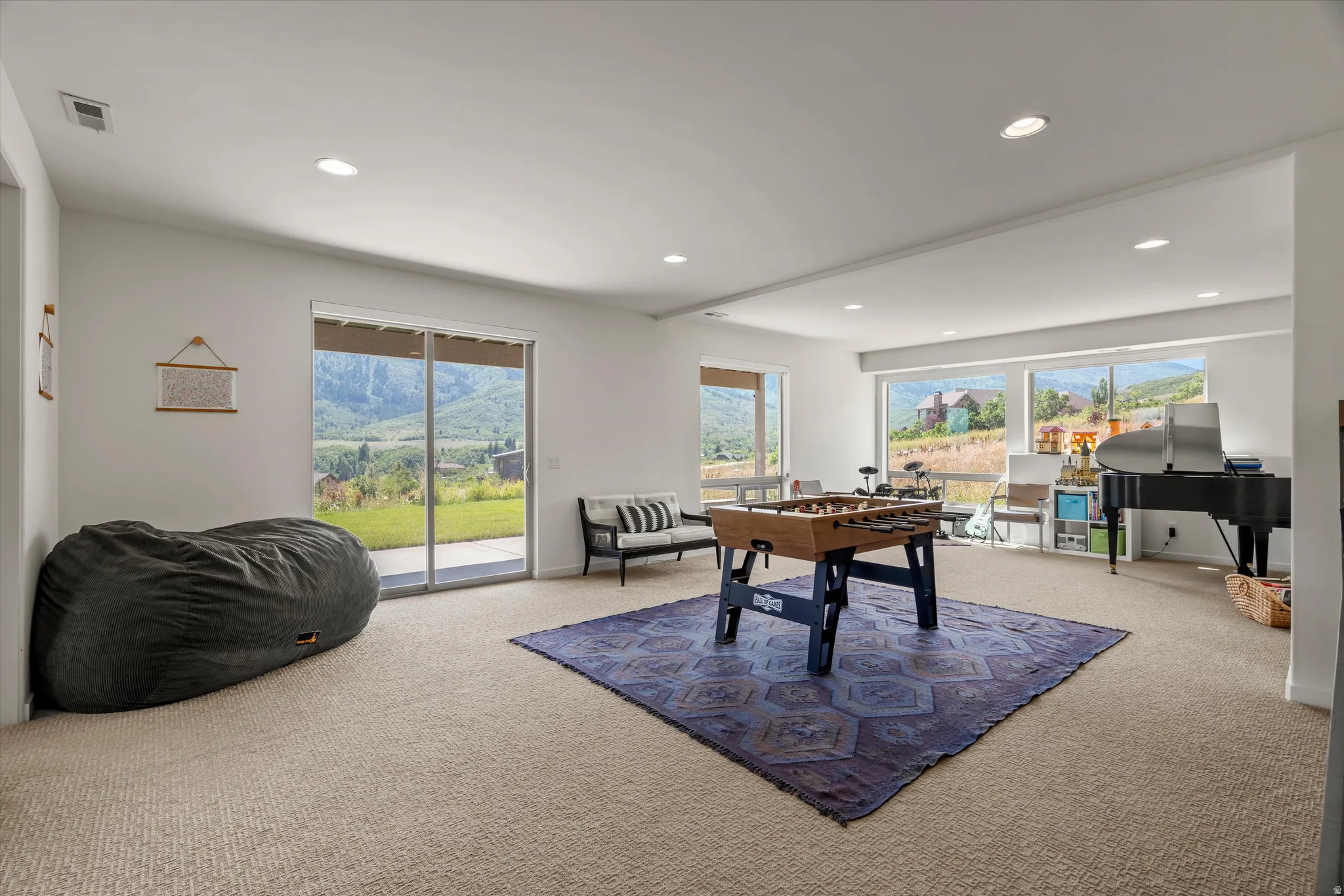 Spacious lower-level room featuring large sliding glass doors, multiple windows, recessed lighting, and soft carpet flooring