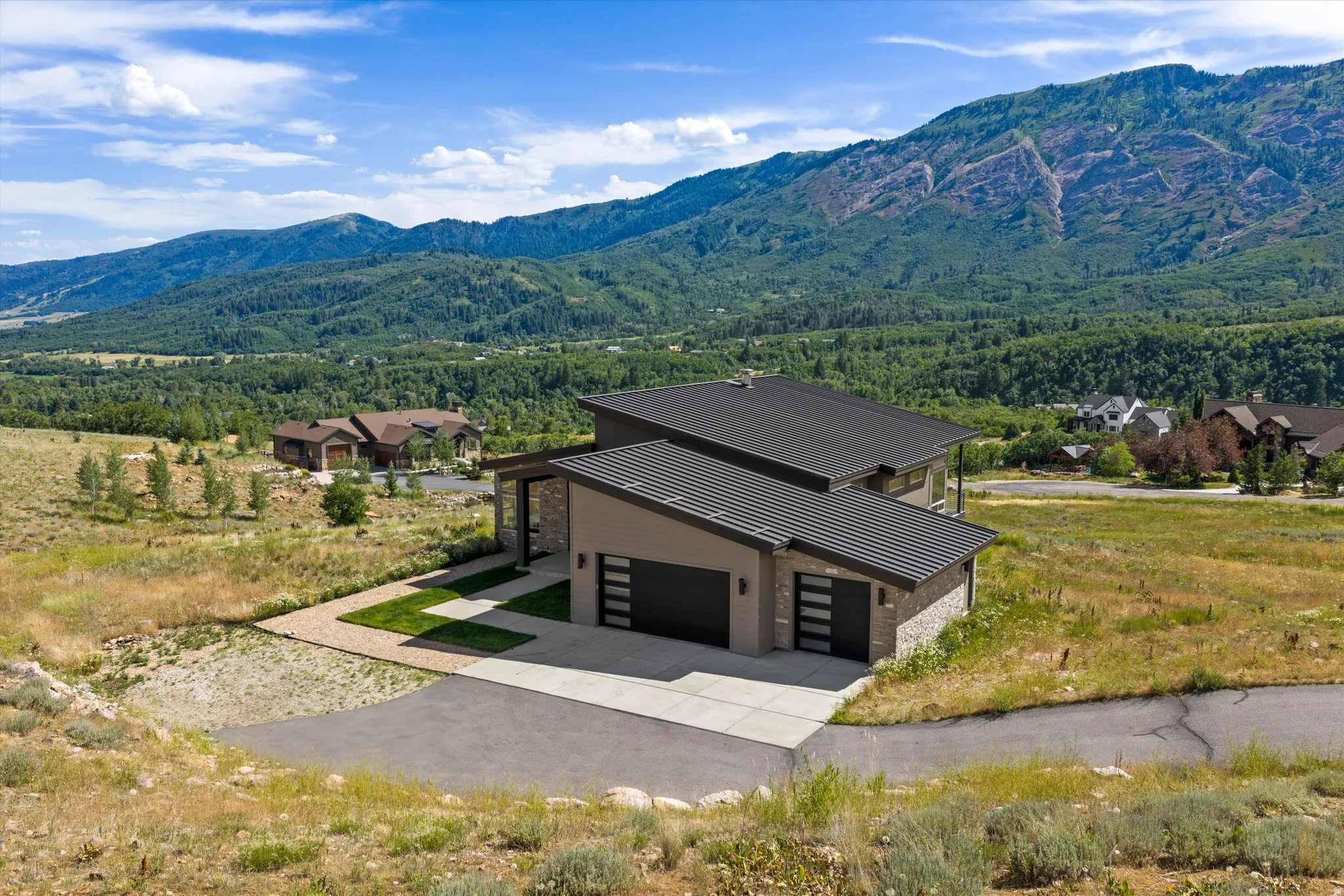 Contemporary mountain home featuring a dark metal roof, a paved driveway, and an attached two-car garage with modern doors