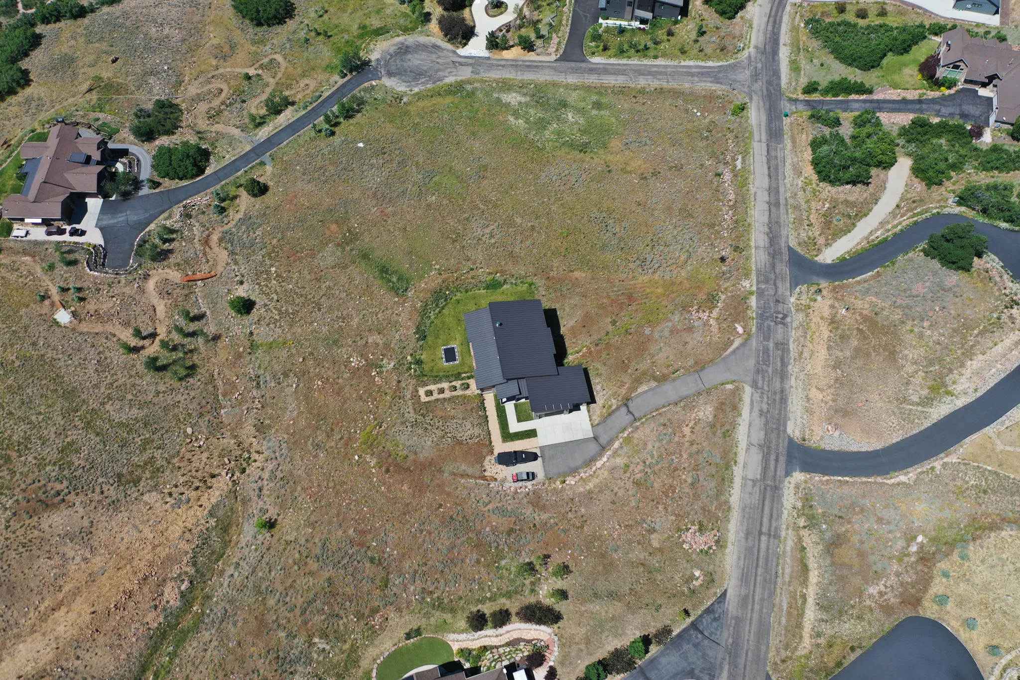 Expansive lot featuring a contemporary residence with a dark roof, private driveway, surrounding undeveloped terrain, and direct street access