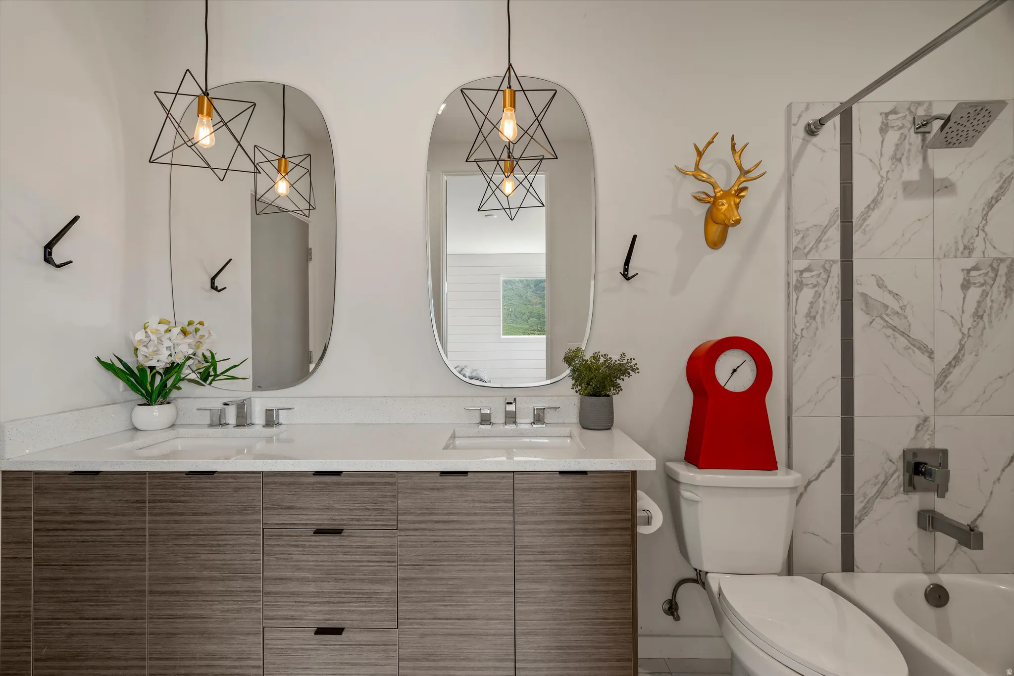 Dual vanity with integrated sinks and wood-finish cabinetry, illuminated by two geometric pendant lights