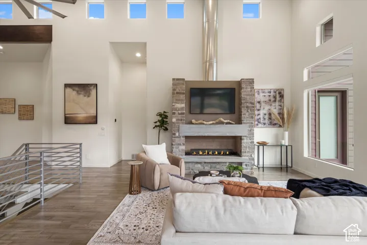 Living area featuring high ceilings, a gas fireplace with stone surround, wood-finish flooring, and multiple windows