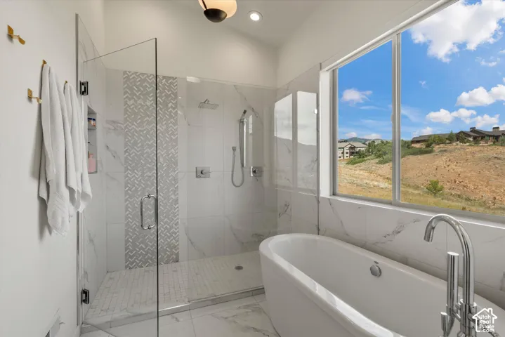 Bathroom featuring a freestanding soaking tub with floor-mounted chrome faucet, a large window, and a glass-enclosed shower with a rain shower head, hand-held shower, and patterned tile accent