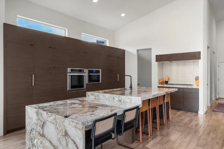 Kitchen featuring extensive dark wood-finish cabinetry, integrated ovens, and two multi-level islands with stone countertops