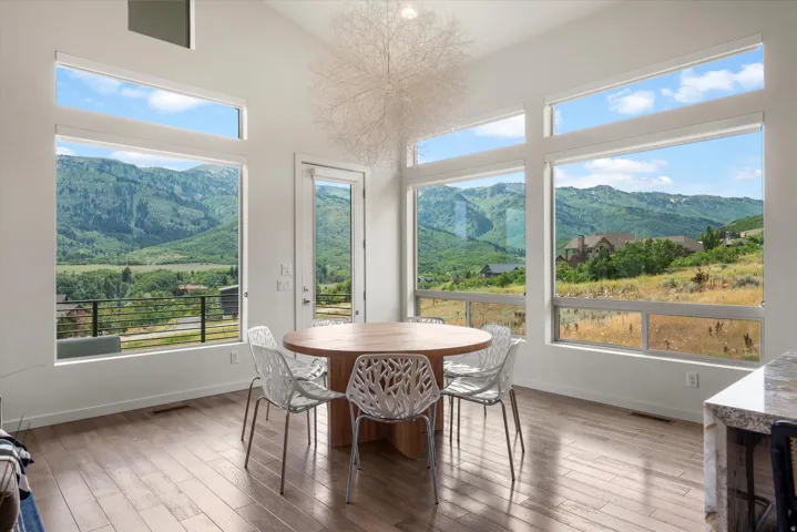 Dining area featuring expansive windows, wood-finish flooring, a modern light fixture, a light-toned wooden table, and a glass-paneled exterior door