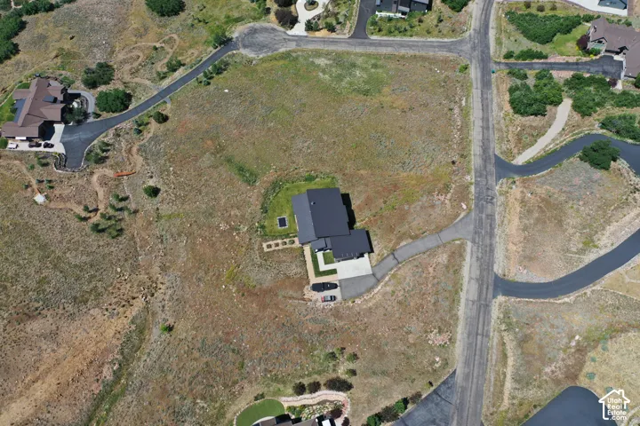Expansive lot featuring a contemporary residence with a dark roof, private driveway, surrounding undeveloped terrain, and direct street access