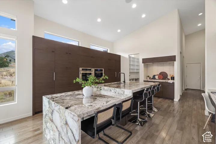 Spacious kitchen featuring a large waterfall-edge island, integrated double ovens, and extensive dark wood-finish cabinetry
