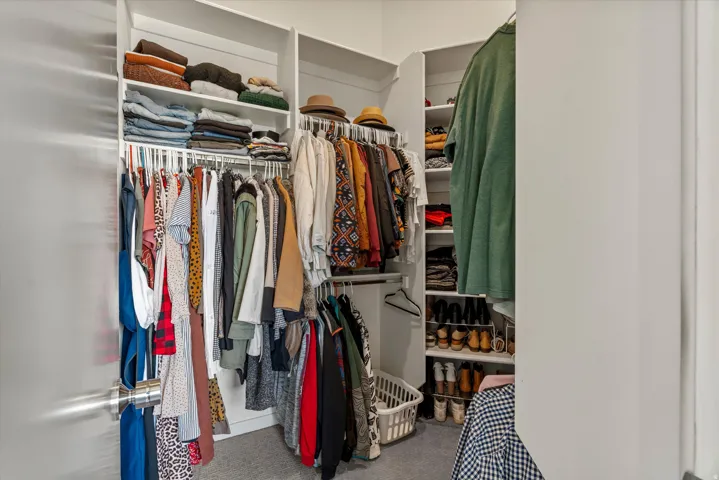 Walk-in closet featuring white built-in shelving, multiple hanging rods, and light gray carpeting
