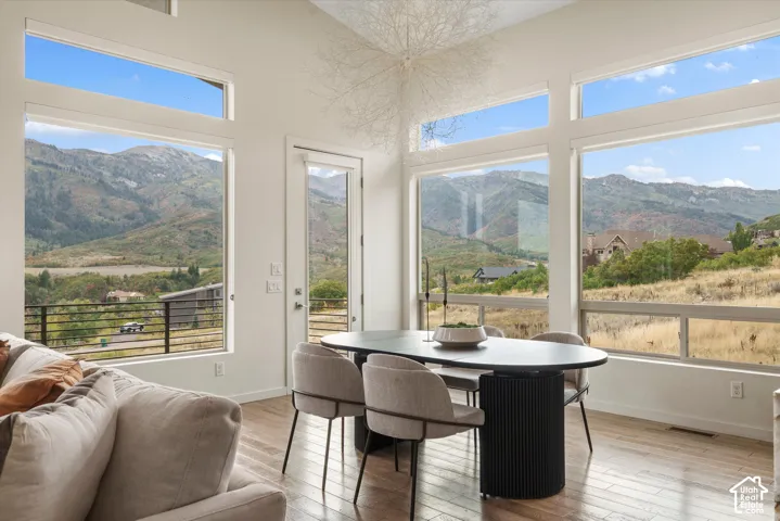 Vaulted ceiling, expansive windows, wood-finish flooring, white walls, and a glass-paneled door
