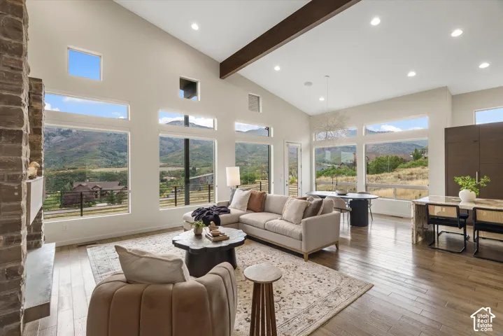 Vaulted ceilings featuring an exposed beam, a stone-clad fireplace, extensive window placement, wood-finish flooring, and recessed lighting