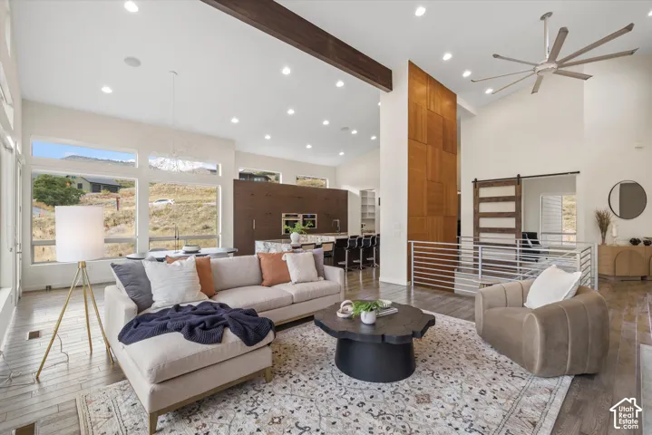 Soaring ceilings with exposed wood beam, expansive window array, wood-finish flooring, contemporary ceiling fan, and modern horizontal bar railing