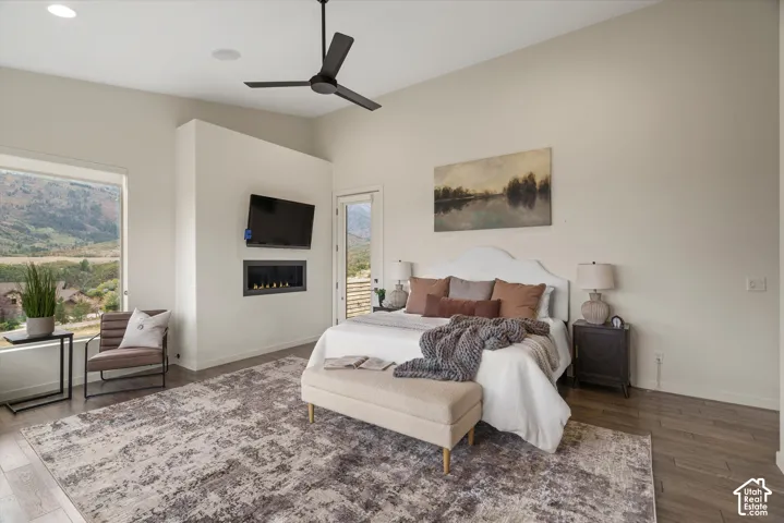 Vaulted ceiling with a flush-mount ceiling fan, built-in linear fireplace, wood-finish flooring, and large picture windows