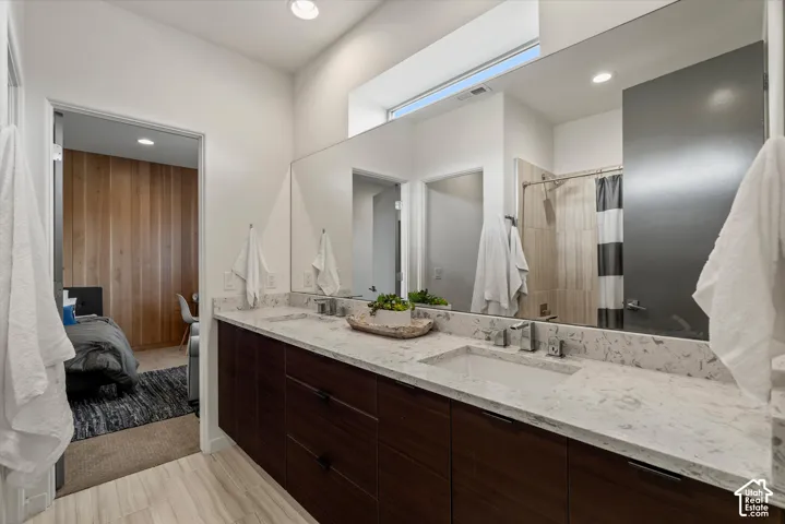 Bathroom featuring a dual-sink vanity with a light-toned countertop, wood-finish cabinetry, and a large wall-mounted mirror