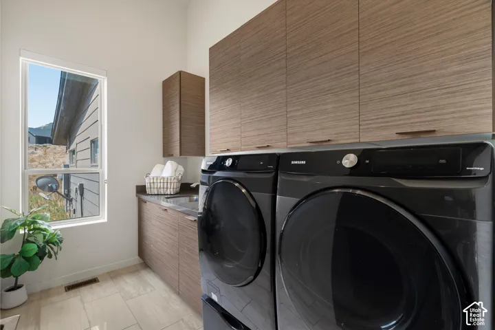 Dedicated laundry area featuring a built-in sink, stone-finish countertop, and ample wood-finish cabinetry