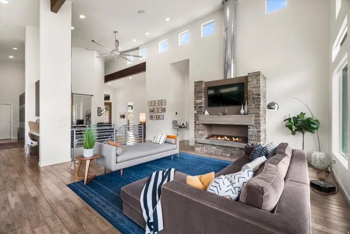 Two-story living area featuring wood-finish flooring, a contemporary stone fireplace with a built-in fire feature, a high ceiling with exposed beams, and multiple clerestory windows