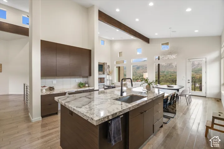 Spacious open-concept interior featuring light wood-finish flooring, high ceilings with exposed wood beams, and a large kitchen island with a stone countertop and an undermount sink