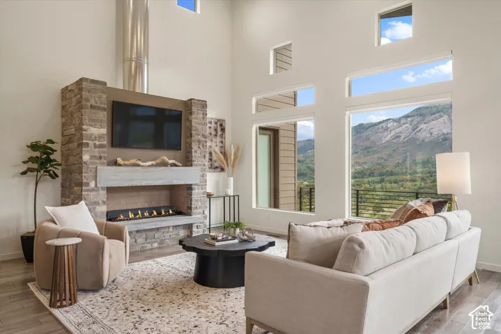 Vaulted ceiling with high windows, stone-clad fireplace with mantel, built-in linear fireplace, wood-finish flooring, and expansive mountain scenery