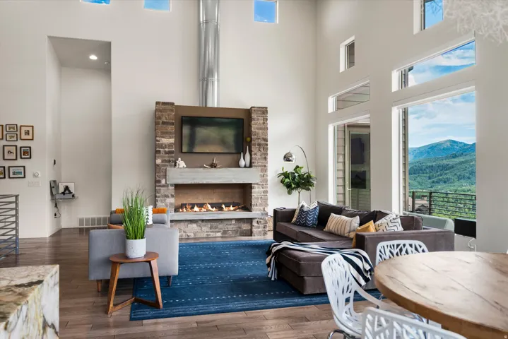 Spacious living area featuring a stone and concrete fireplace with integrated media space, high ceilings, large floor-to-ceiling windows, and wood-finish flooring