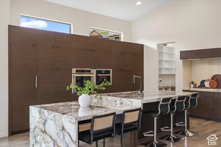 Integrated stainless steel appliances, wood-finish cabinetry, granite island countertop with waterfall edge, built-in shelving, and transom windows